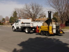 A dump truck is shown on the street towing an asphalt recycler.