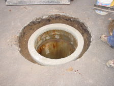 A sewer manhole is shown with a new grade ring and ready for installation of the ring and lid.