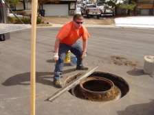 A worker is shown checking the level of the sewer manhole ring and lid.