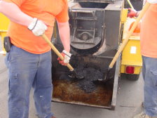 Workers are shown removing hot asphalt from the recycler with a shovel.